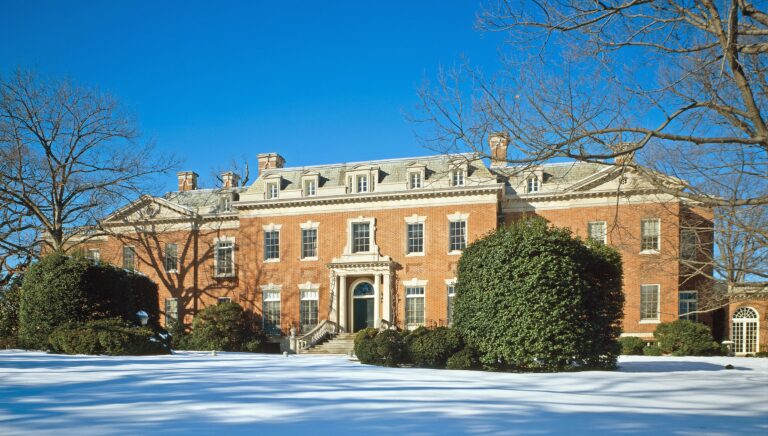 Dumbarton oaks, one of Washington DC's best places to visit with amazing gardens and art exhibitions, is pictured here with one of its red-brick buildings on a sunny, snowy day in winter.