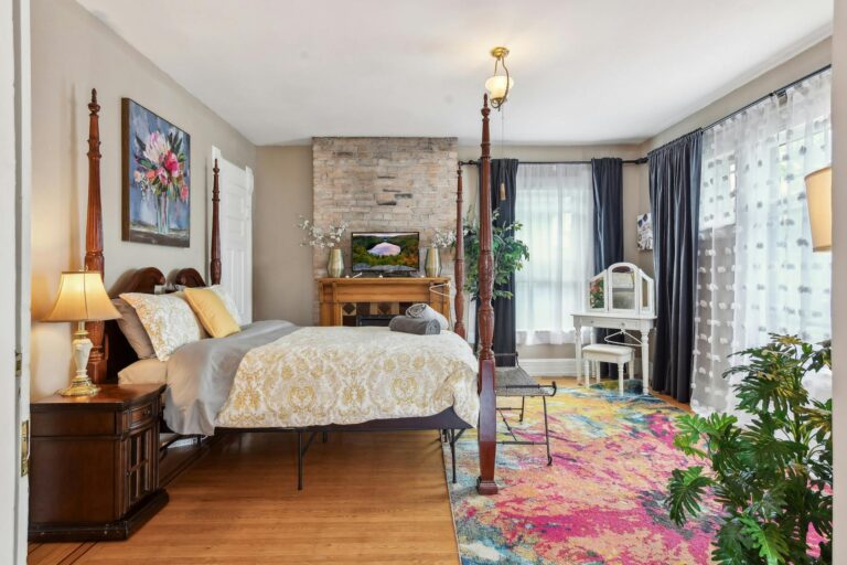Luxurious master bedroom in the Harry F. Legg House, featuring high ceilings, elegant furnishings, and ample natural light streaming through stained-glass windows.