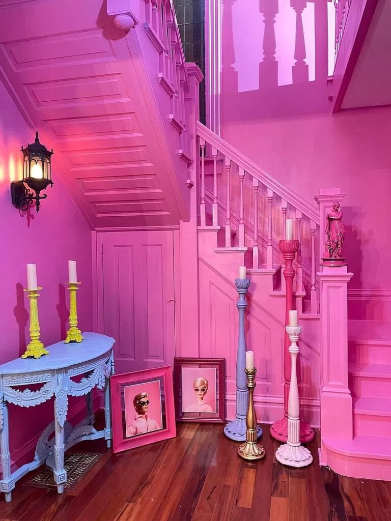 Charming pink wooden staircase in the Barbiecore Mansion, showcasing intricate craftsmanship and a whimsical design that adds to the home's playful aesthetic.