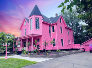 Exterior view of the Barbiecore Mansion, showcasing its vibrant pink facade and charming architecture, surrounded by lush greenery.