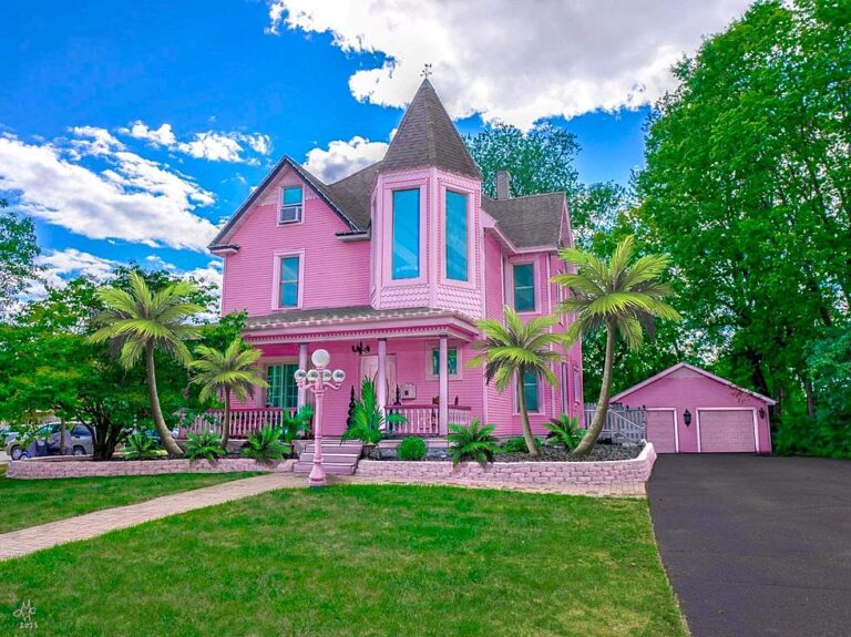 Exterior view of the Barbiecore Mansion, showcasing its vibrant pink facade and charming architecture, surrounded by lush greenery.
