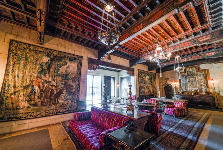 Cozy yet regal sitting area inside Hearst Castle, adorned with rich tapestries, a grand fireplace, and European decor accents.