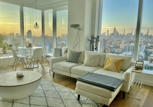 A spectacular apartment to stay in New York City for visitors, this New York apartment has views of downtown and is modern, with white walls, accents, and furniture, making it feel even more spacious and chic.